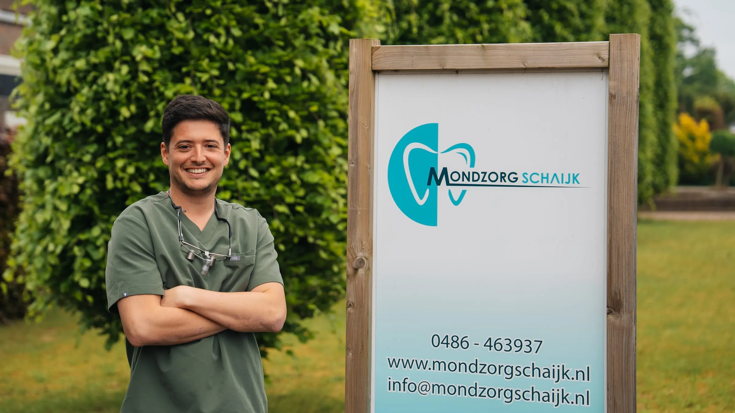 Tandarts Monir bij het bord van Mondzorg Schaijk voor de praktijk